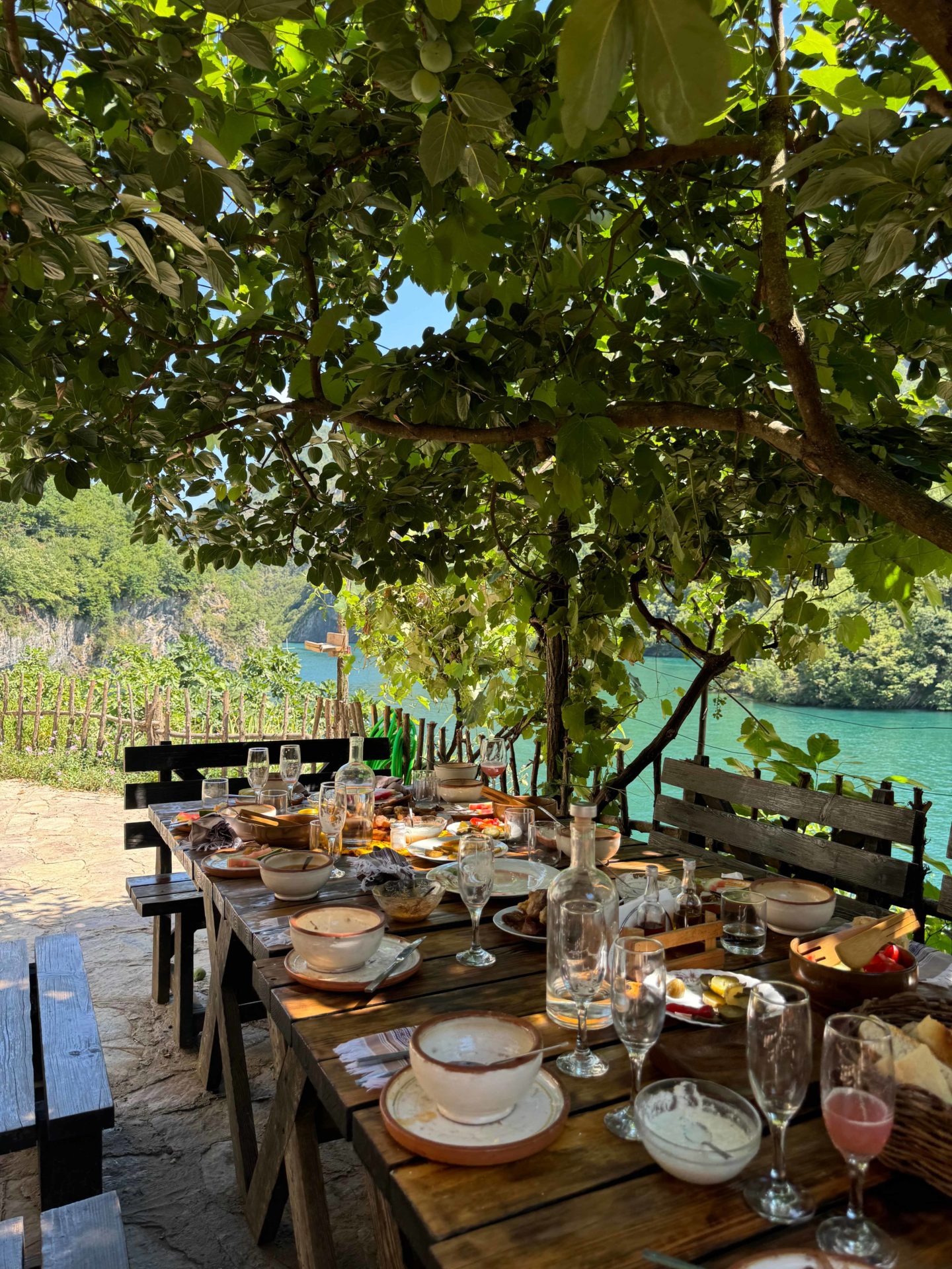 A table set up for lunch outside in Albania, next to a lake and under a tree