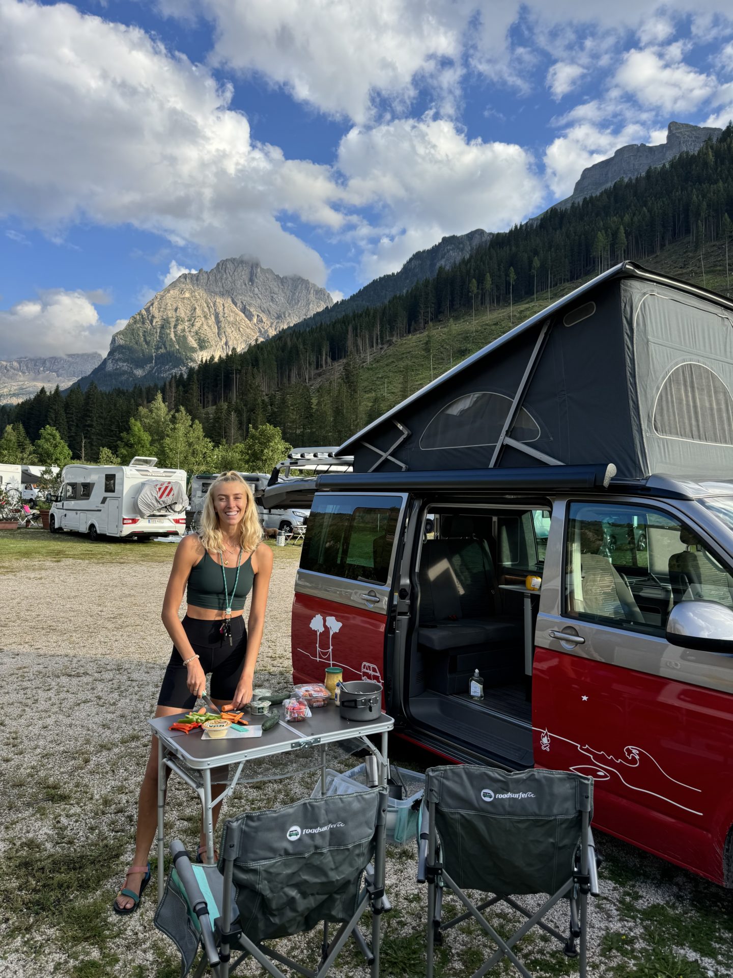 Zanna van Dijk stands next to her Roadsurfer camper van preparing food in the Dolomites